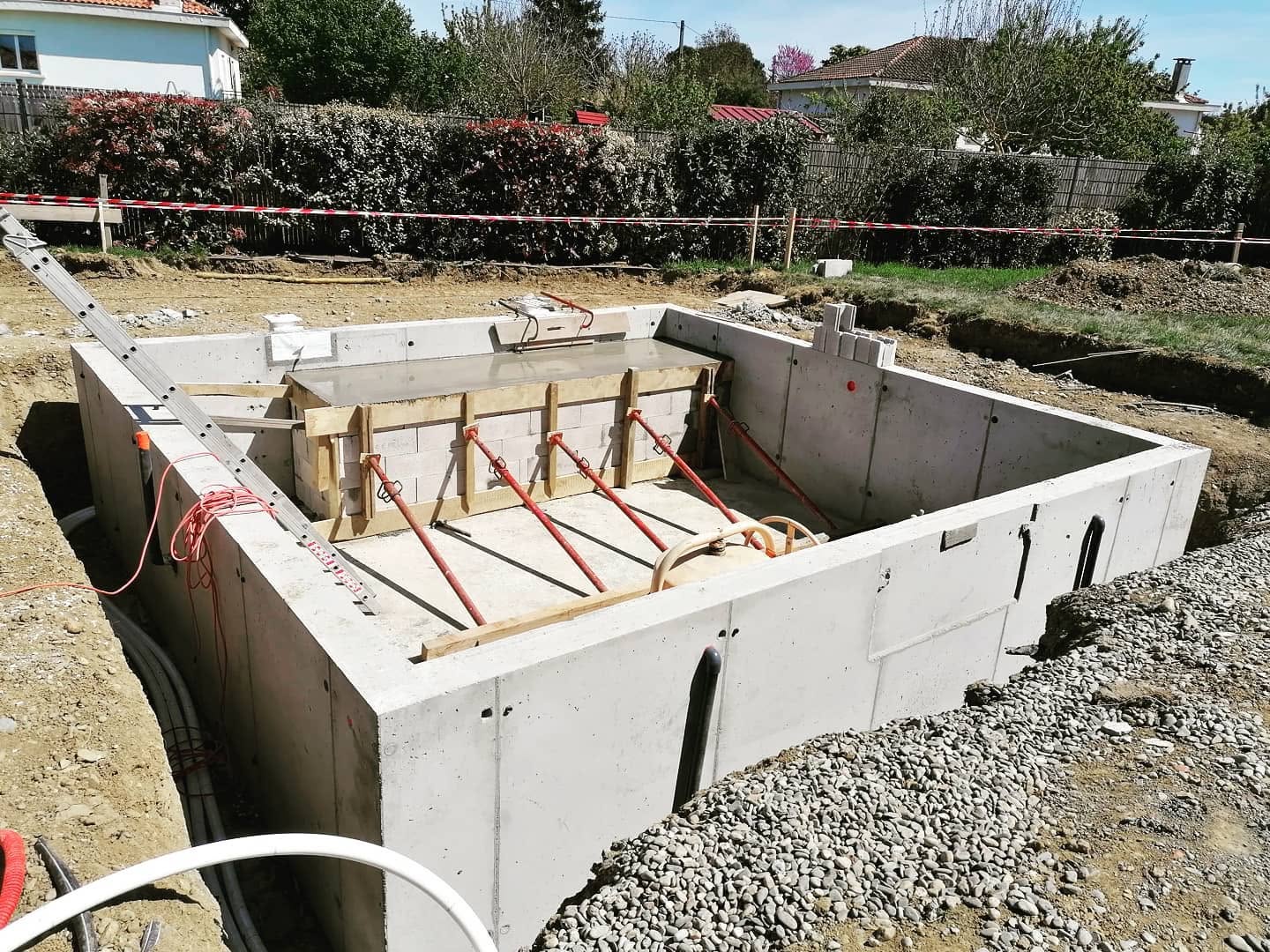 Chantier de piscine en béton armé avec murs banchés, étais de soutien rouges et coffrage en cours.