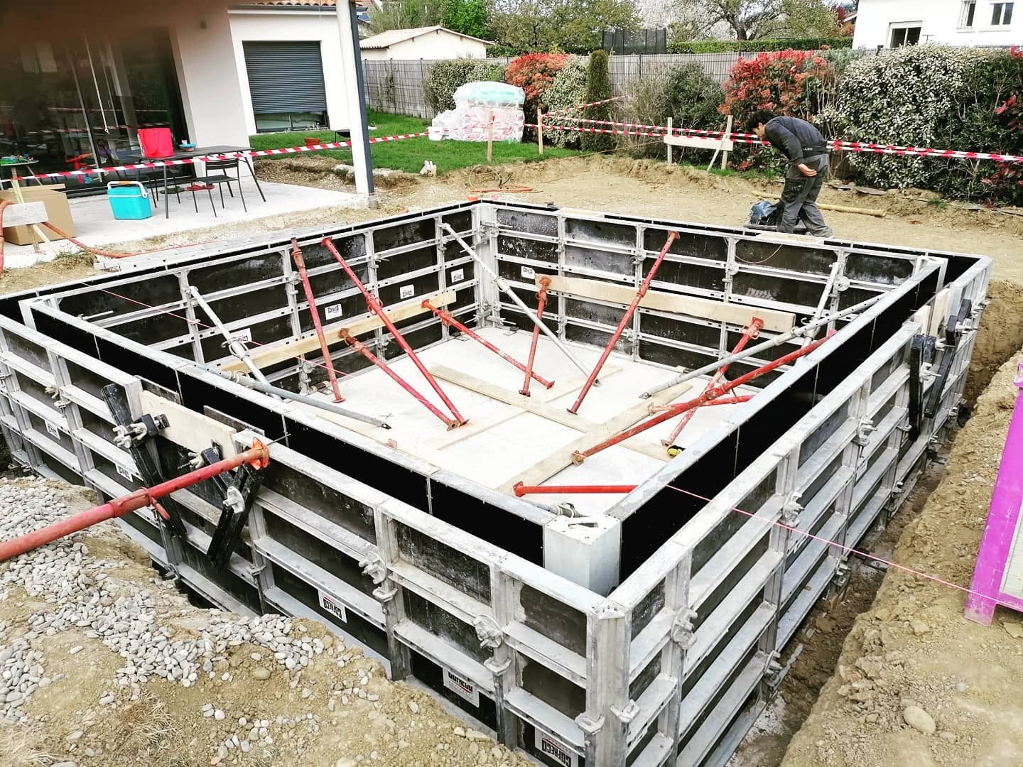 Coffrage métallique COFRECO et étais rouges pour construction de piscine dans un jardin.