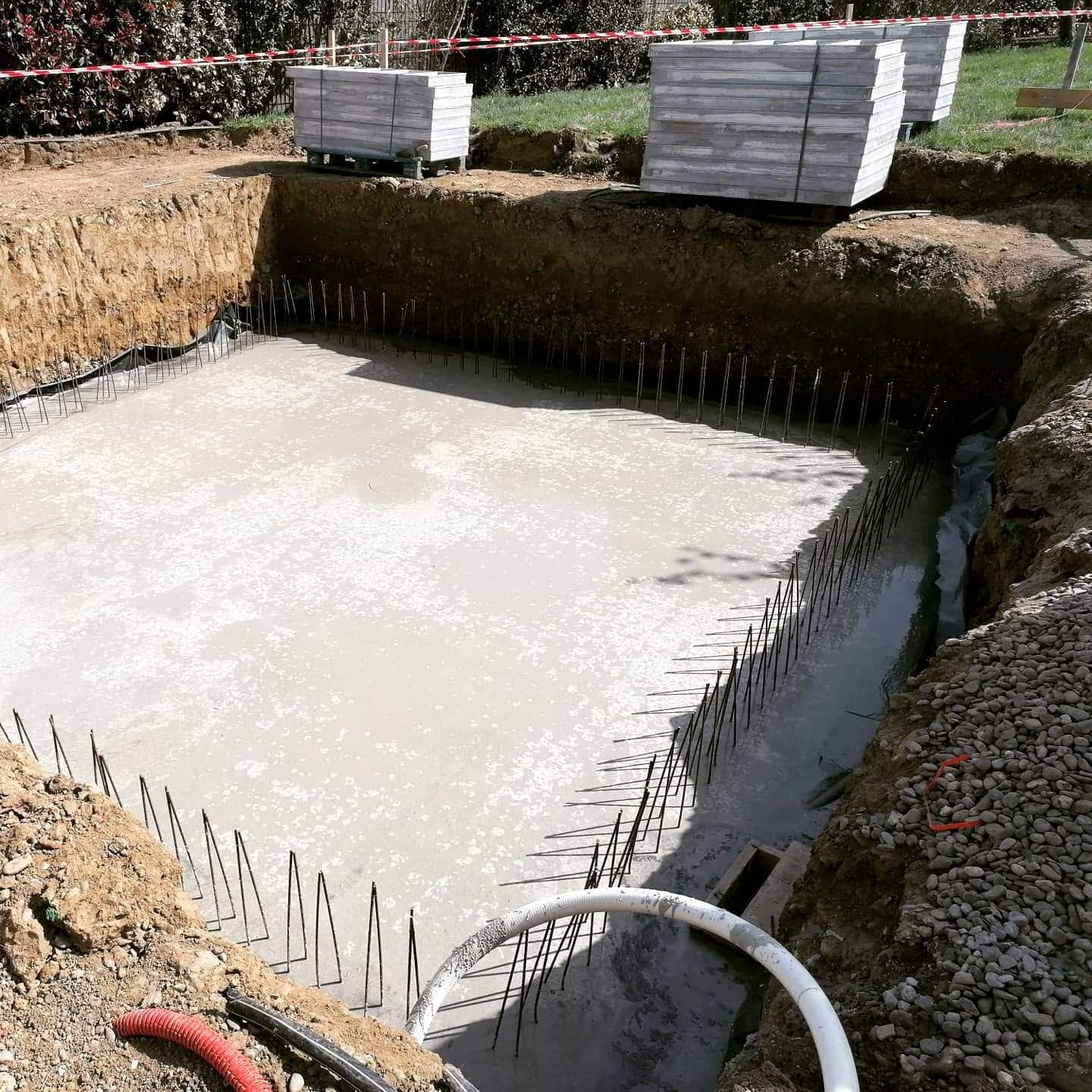 Dalle en béton frais dans une fosse d'excavation avec fers à béton verticaux pour fondation de piscine.