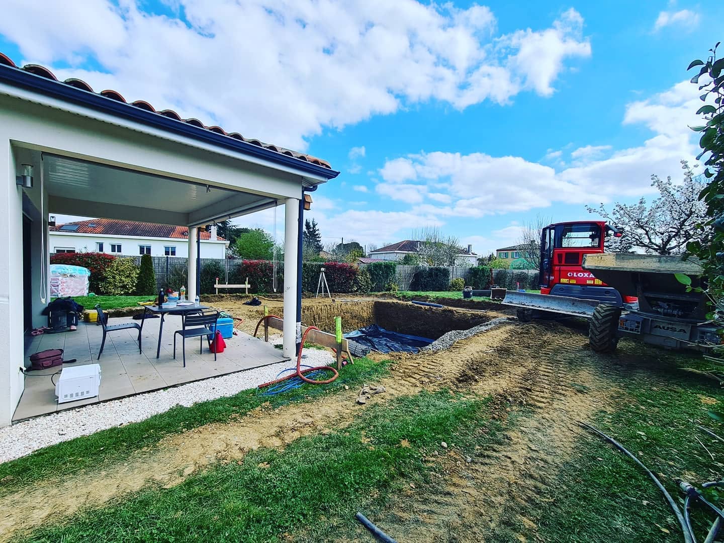Chantier de piscine avec mini-pelle Loxa AUSA et terrassement de jardin devant une maison moderne.