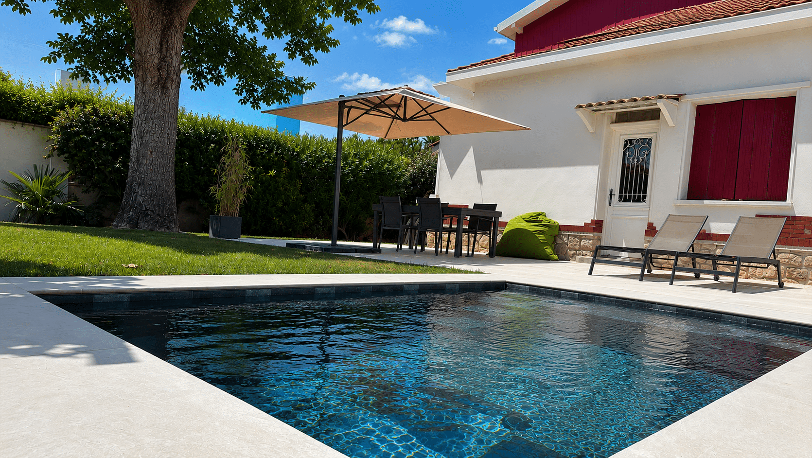 Piscine moderne et terrasse équipée avec parasol et transats devant une maison ensoleillée.