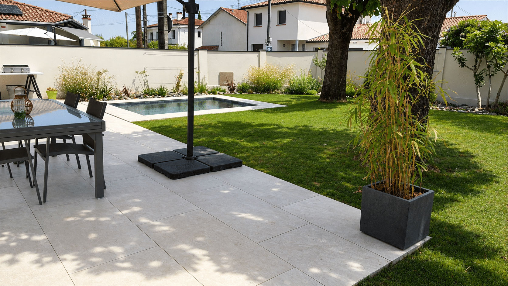 Terrasse moderne avec dalles claires, piscine, salon de jardin et pelouse ensoleillée.